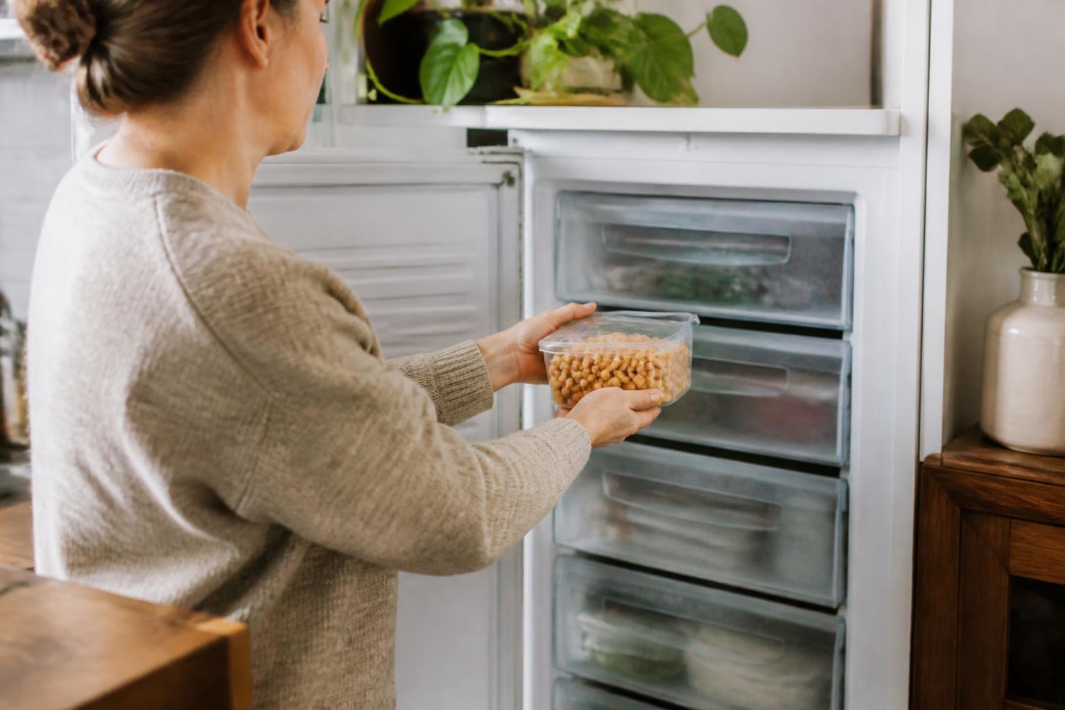 A glass bowl filled with cooked chickpeas sits on a wooden kitchen counter next to a freezer-safe storage bag