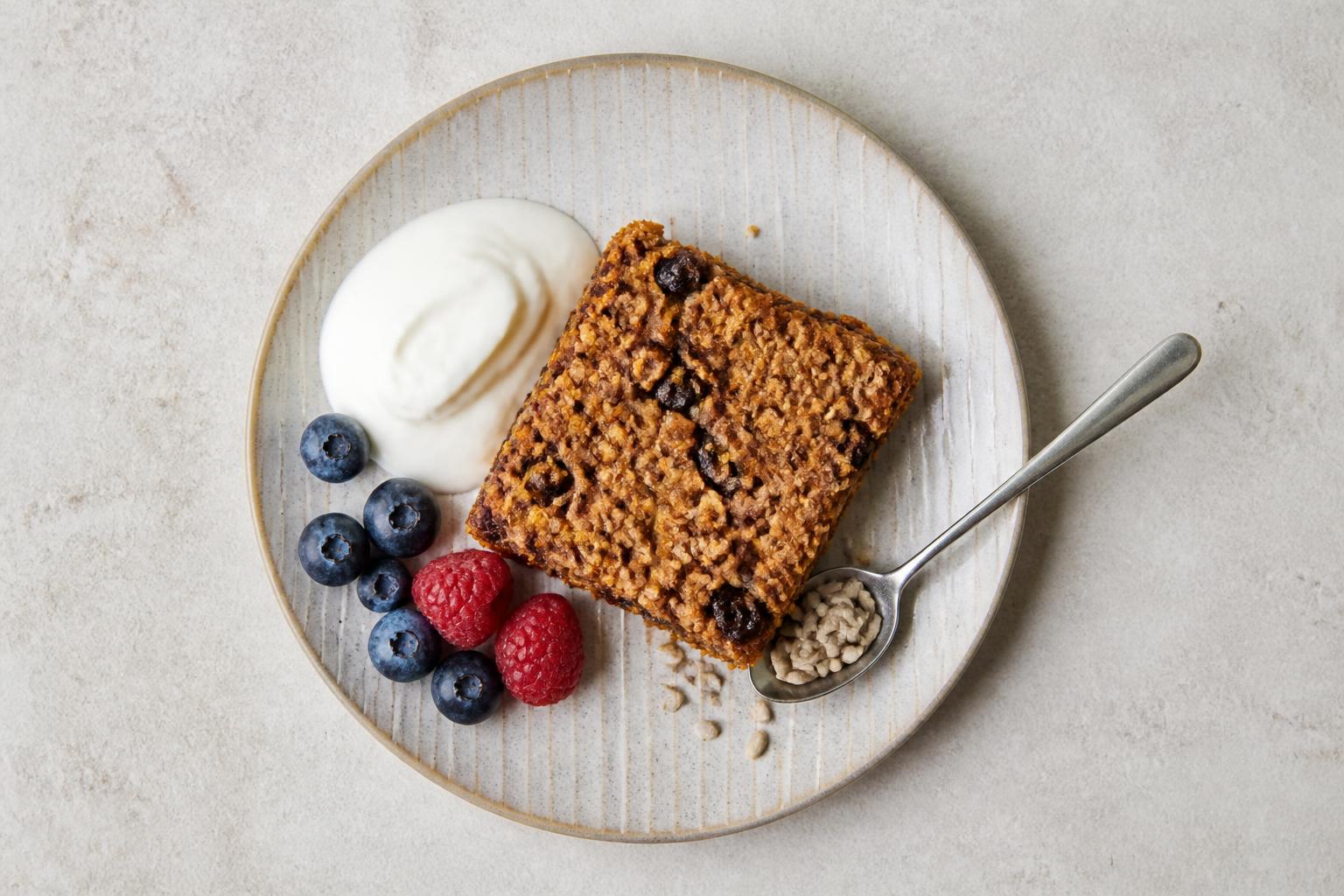 A stack of oat flapjacks topped with fresh berries and seeds on a rustic wooden table