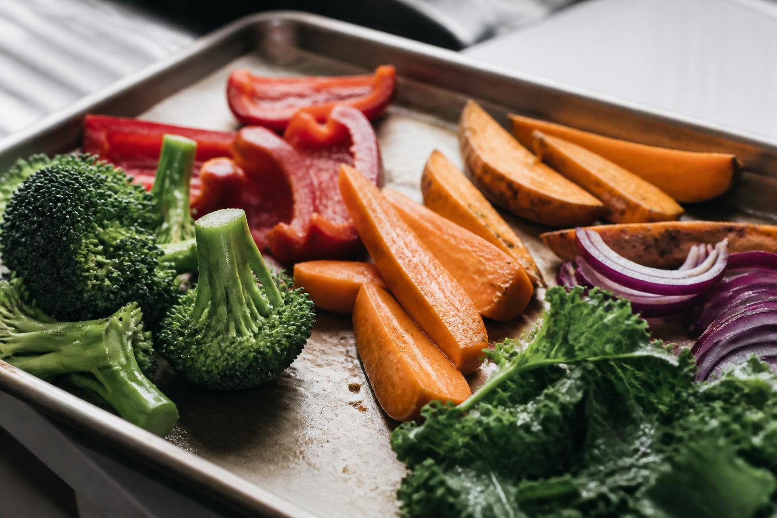A wooden table arranged with colorful fresh vegetables including carrots, spinach, bell peppers and sweet potatoes