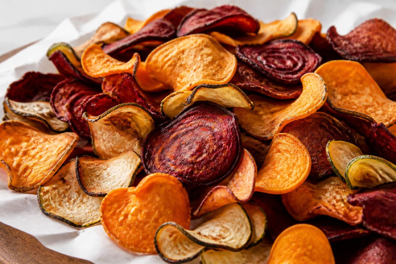 Thinly sliced colorful root vegetables arranged in a single layer on a parchment-lined baking sheet