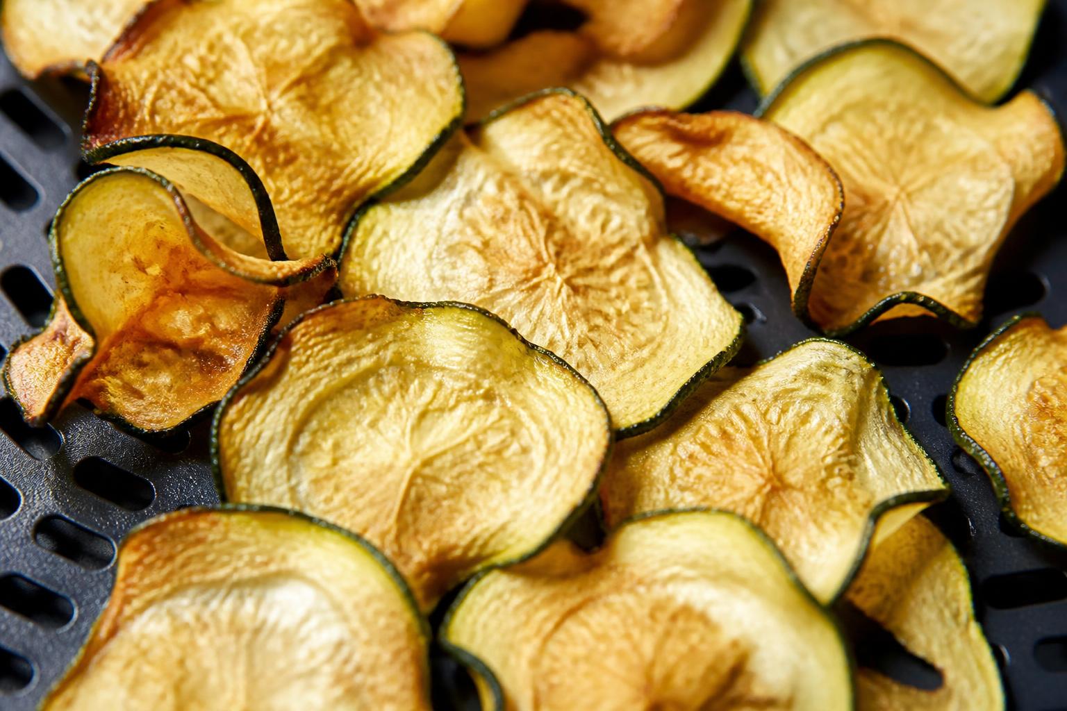 Thinly sliced colorful raw vegetables arranged neatly on a wooden cutting board before air frying