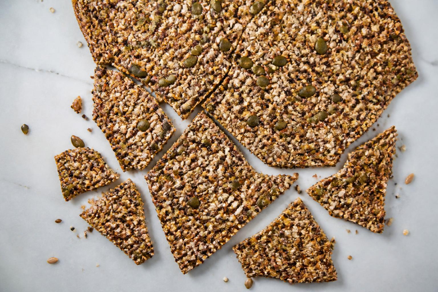 Golden-brown seed crackers arranged neatly on a rustic wooden board next to a small bowl of sea salt