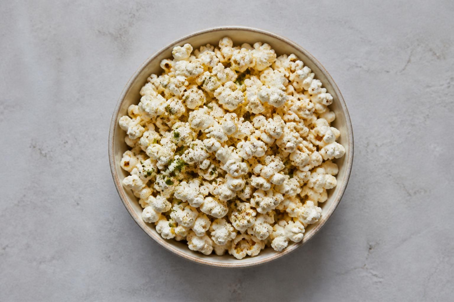 A large glass bowl overflowing with golden, buttery popcorn sits on a rustic wooden table