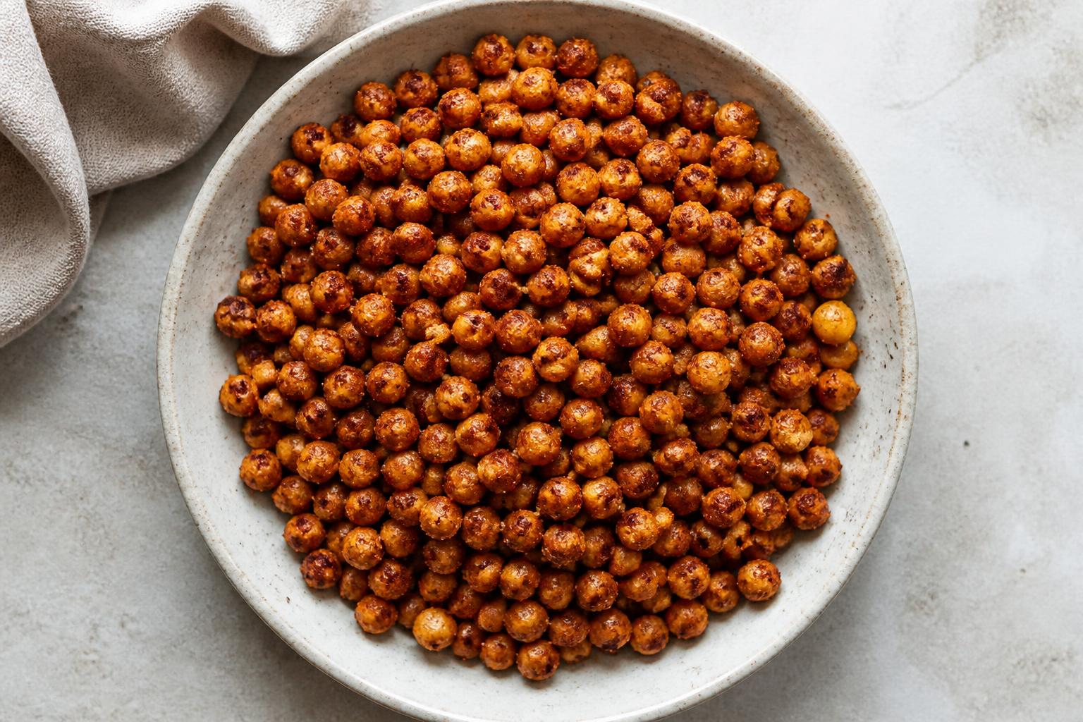 Golden-brown roasted chickpeas scattered across a dark baking sheet lined with parchment paper