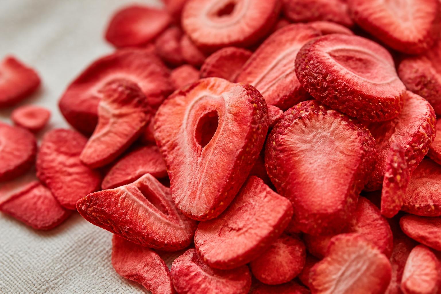 A vibrant assortment of freeze-dried strawberry slices and blueberries scattered across a white surface