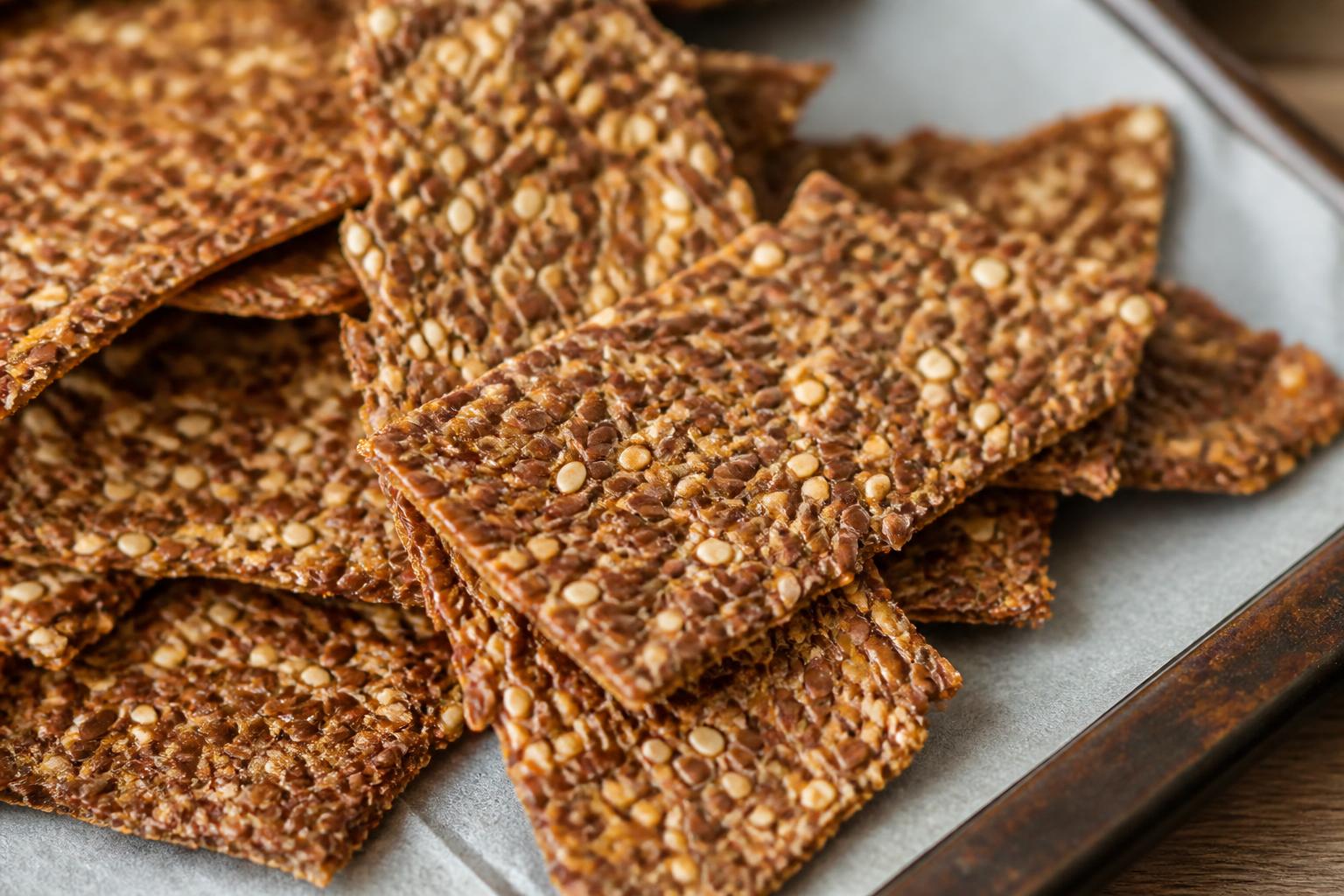 Crispy golden flax seed crackers arranged on a rustic wooden board with scattered whole seeds nearby