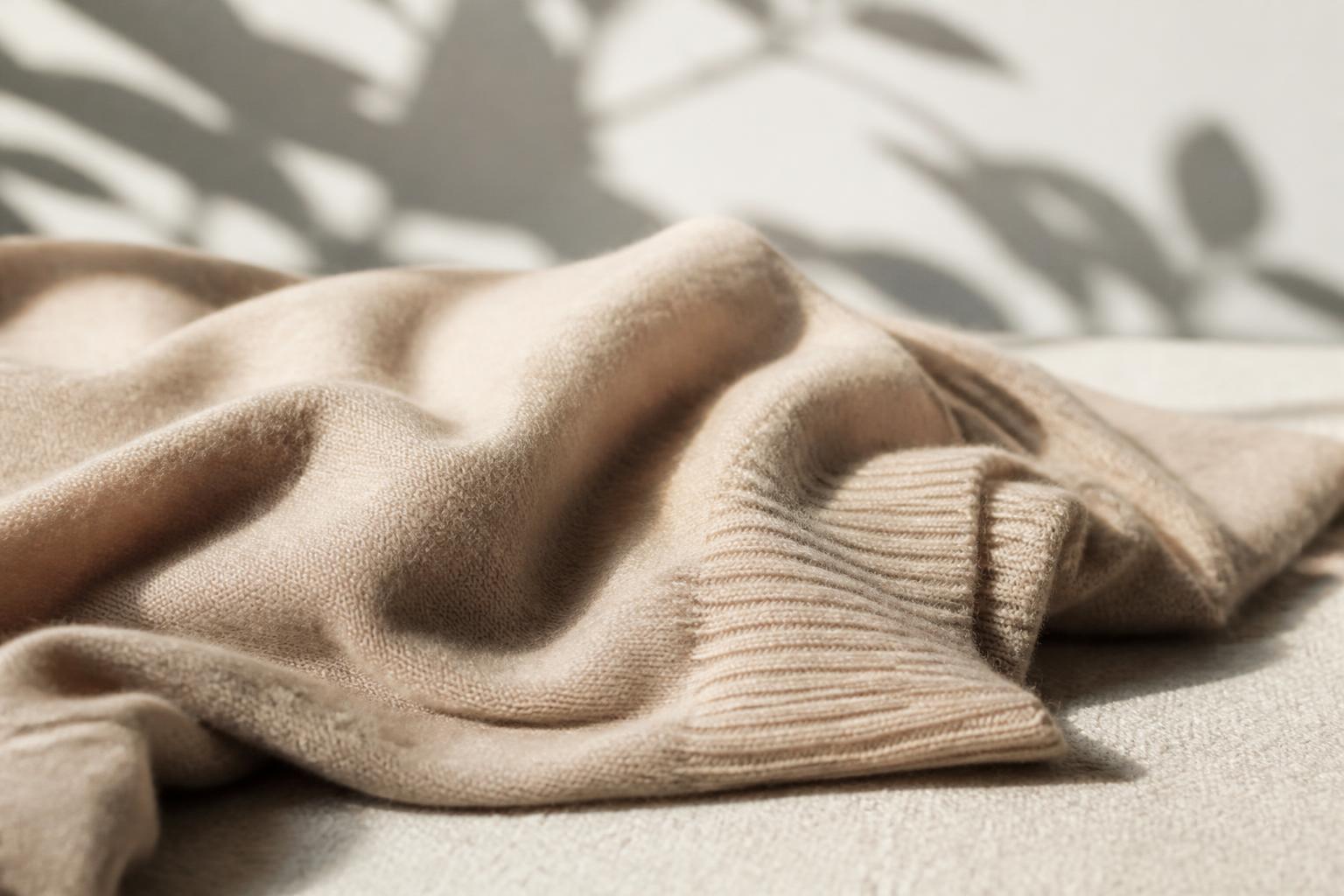 A close-up of a soft, folded beige cashmere sweater resting on a wooden surface