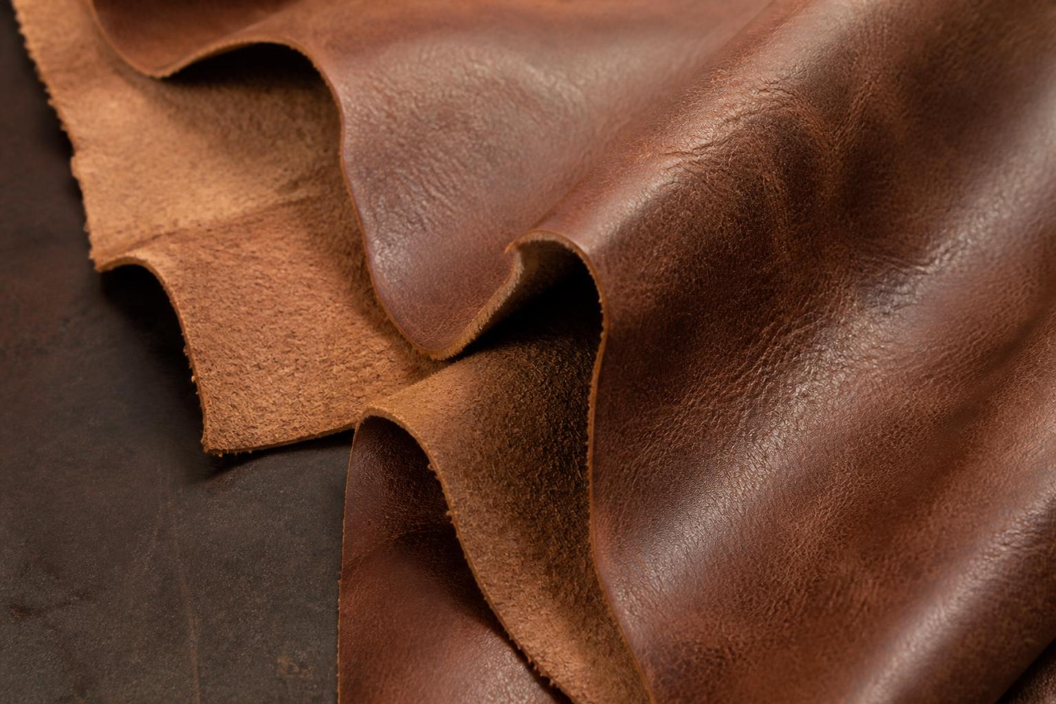 A stack of raw, tanned leather hides laid out on a wooden table in a sunlit workshop
