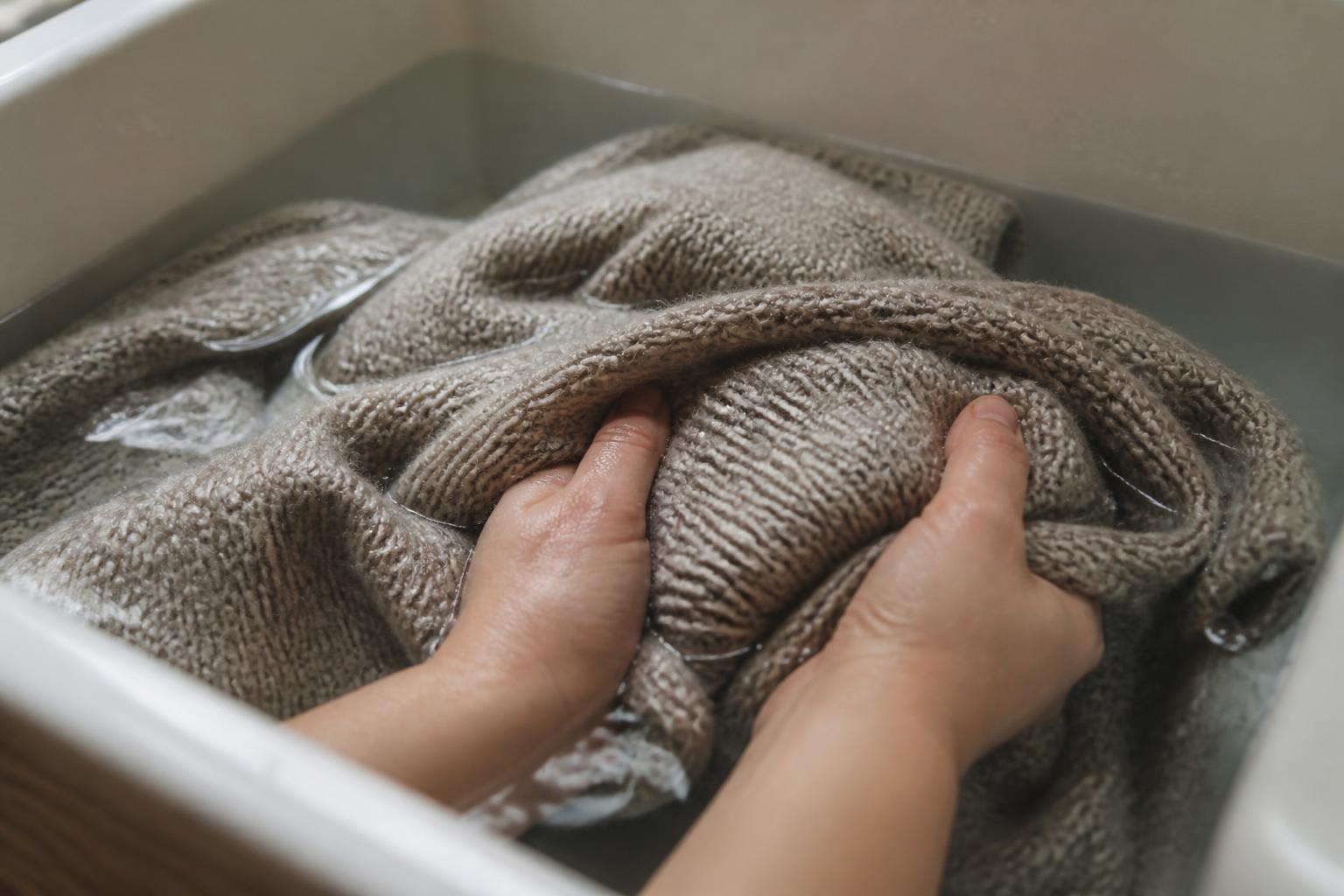 A neatly folded beige wool jumper resting on a wooden surface beside a soft knit blanket