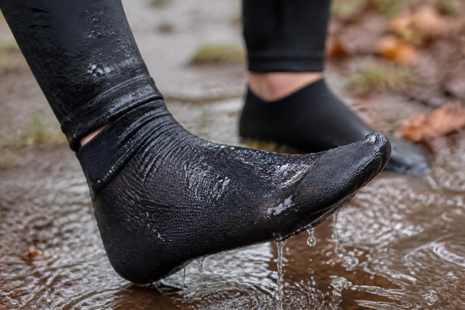 A pair of waterproof running socks resting on a damp, muddy trail path surrounded by autumn leaves